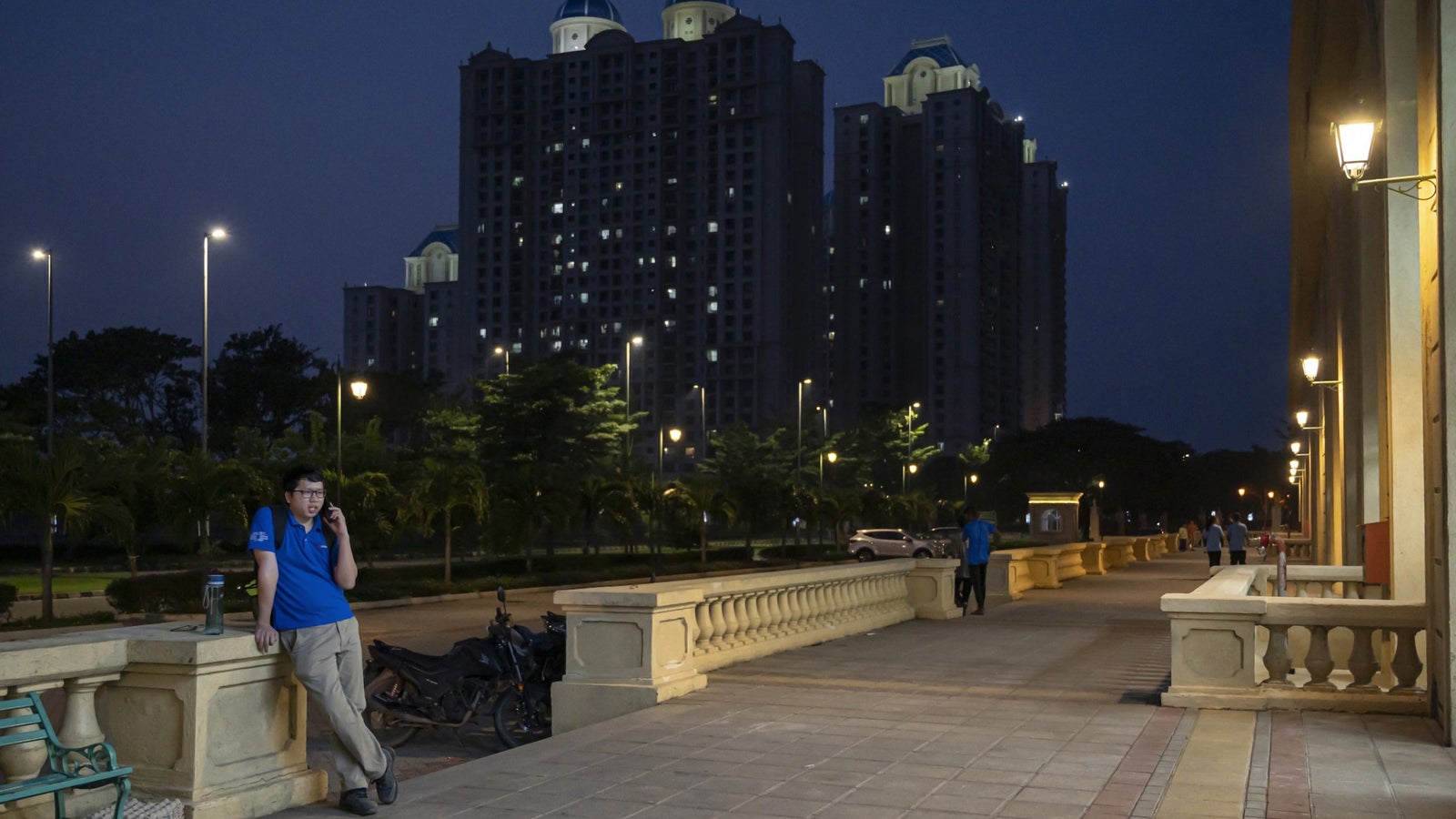A photo showing a night scene outside an upscale apartment complex with a man talking on a phone and other people milling about.