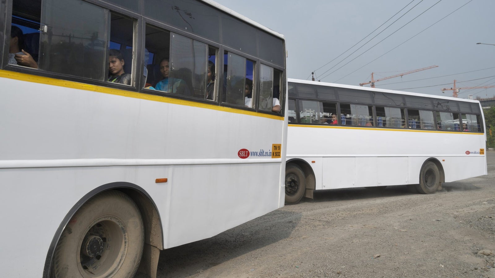 A photo showing two buses, filled with people, driving on a dirt road.