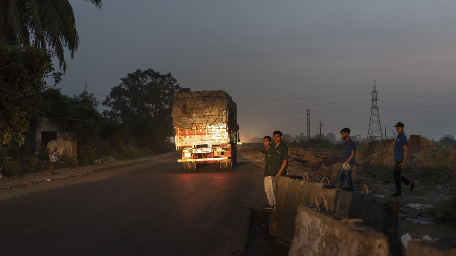 A photo showing people waiting by the side of the road during twilight.
