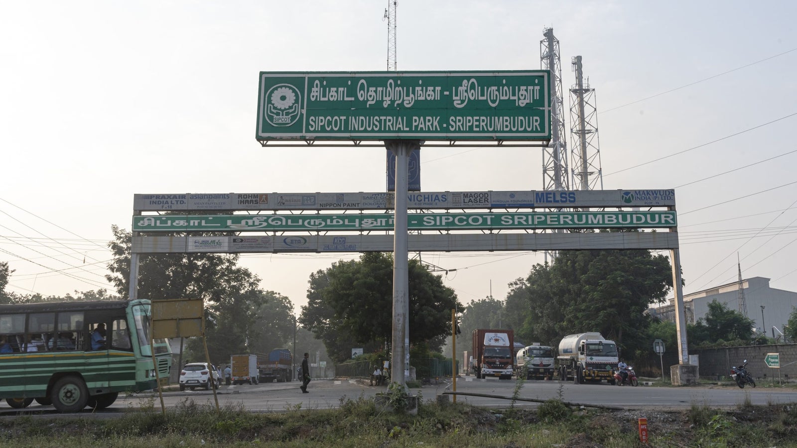 A photo showing a set of road entrance billboards in English and Hindi with buses, cars, and trucks on the roads below it.