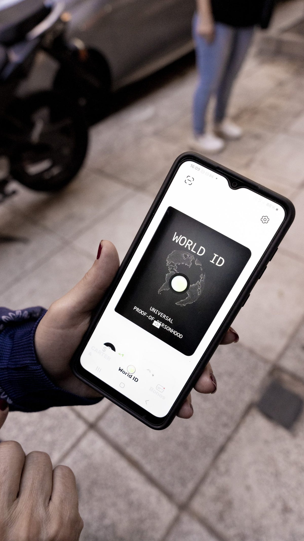 A hand holds a phone showing the Worldcoin World ID on the screen.