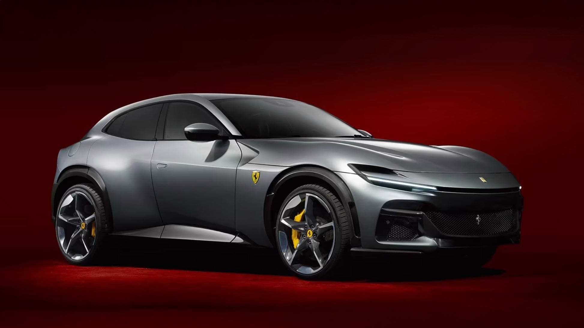 Главный серый автомобиль Ferrari, демонстрирующий спортивный дизайн с выдающейся передней решеткой, смелыми фарами и отличительными колесами с желтыми акцентами, расположенными на богатом красном фоне.
