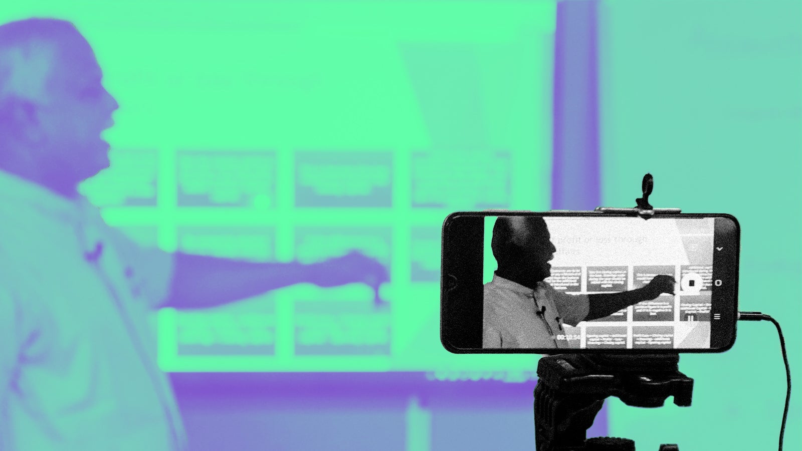 A presenter gestures animatedly while being filmed on a smartphone, with a presentation displayed in the background.