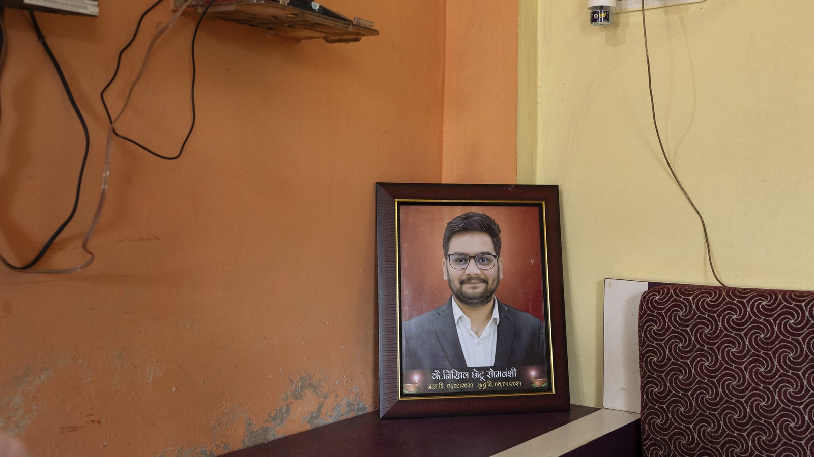 A framed portrait of a young man in a suit, placed on a table against an orange wall.