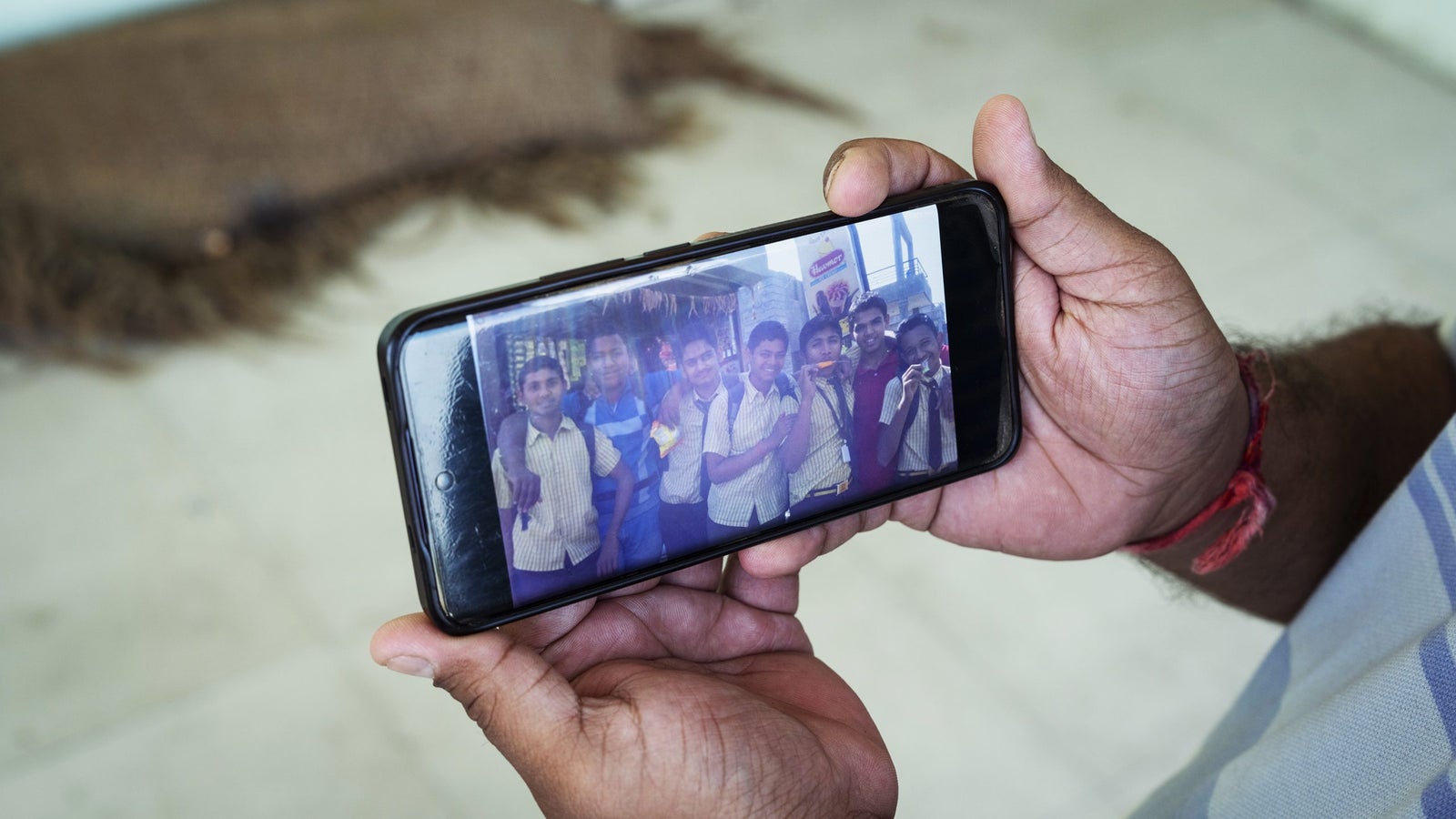 A person holds a smartphone displaying a photo of several smiling students posing together.