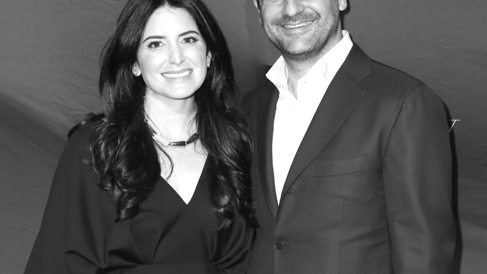 A couple poses together, smiling, at a 92NY event, dressed in formal attire against a branded backdrop.