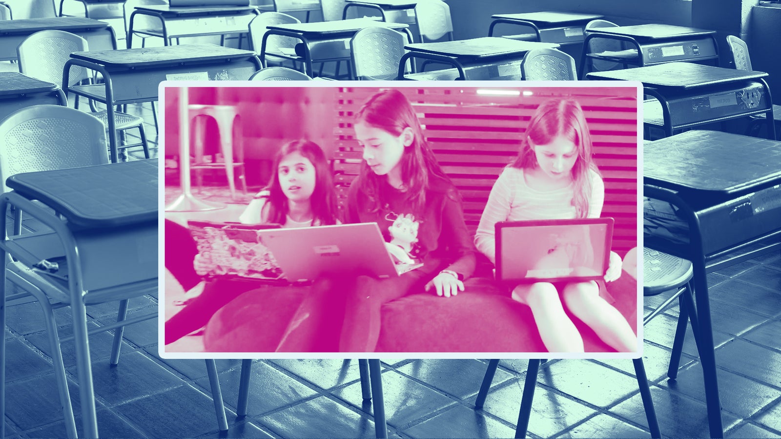 Three girls sit together on a couch, focused on their laptops, with classroom desks in the background.
