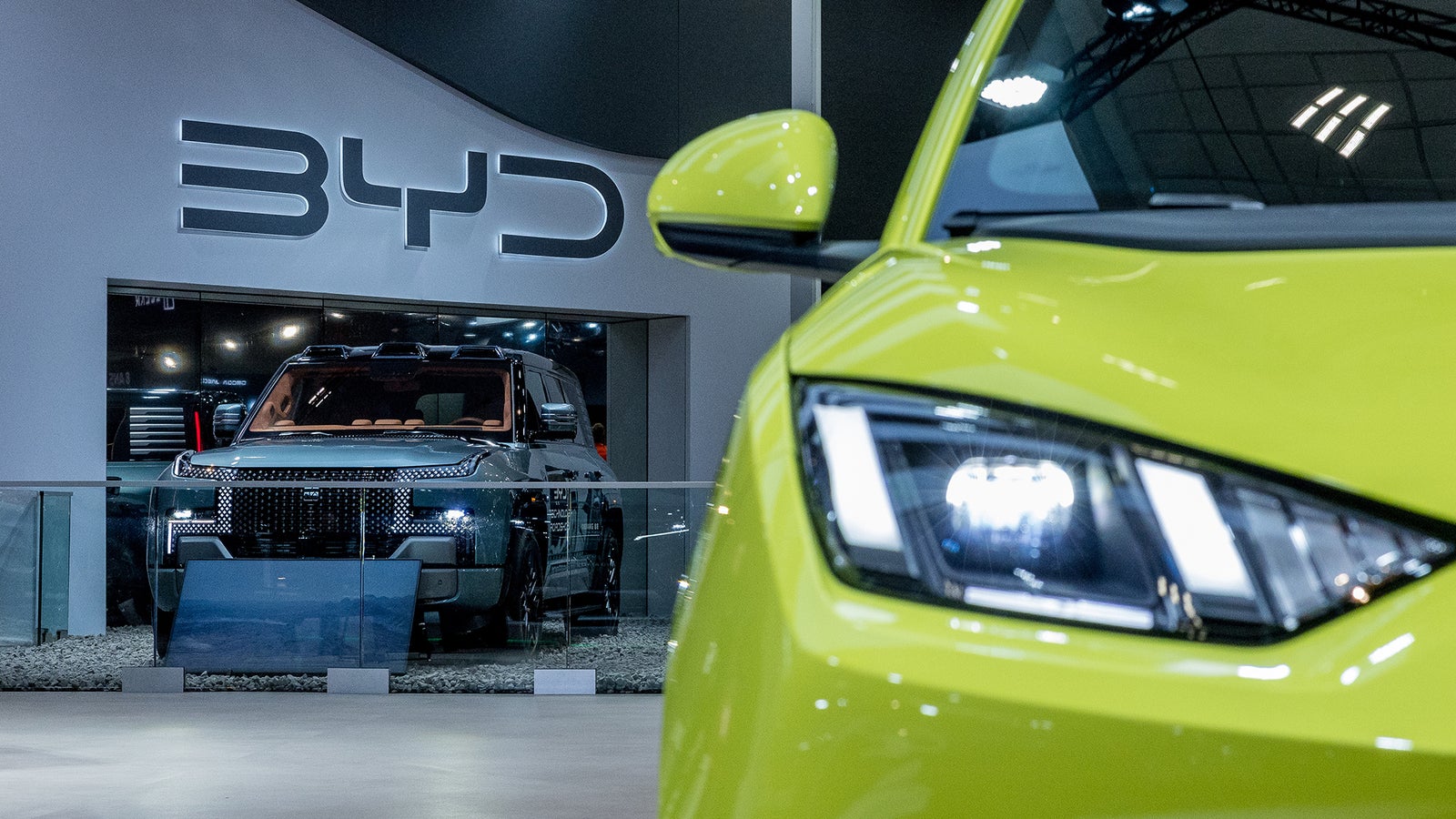 A close-up of a bright green car's front, with a dark SUV in the background, displayed at a car show.