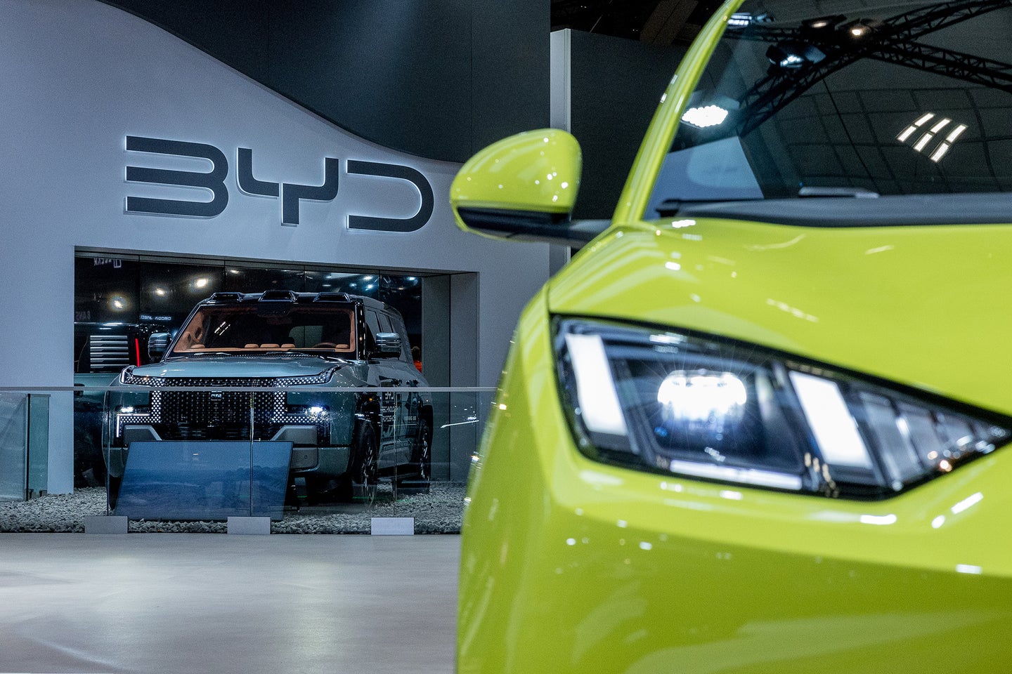 A close-up of a bright green car's front, with a dark SUV in the background, displayed at a car show.