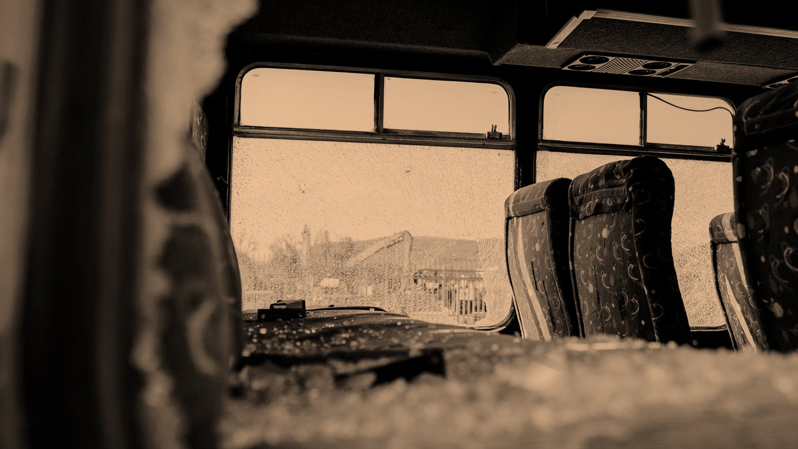 Interior of a bus with shattered windows, revealing broken glass and empty seats.