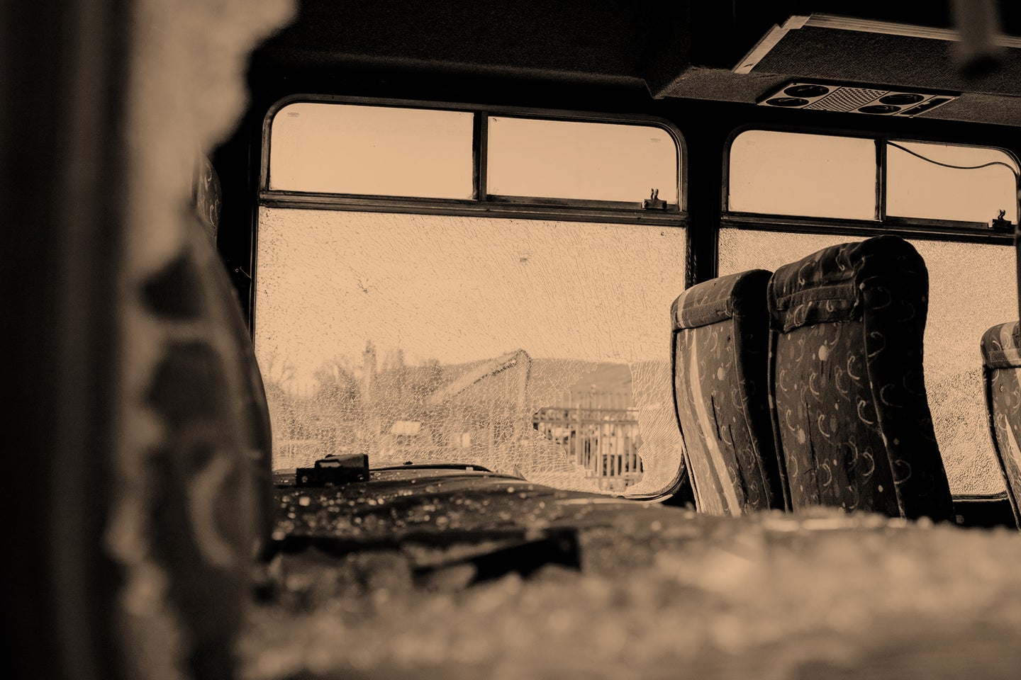 Interior of a bus with shattered windows, revealing broken glass and empty seats.