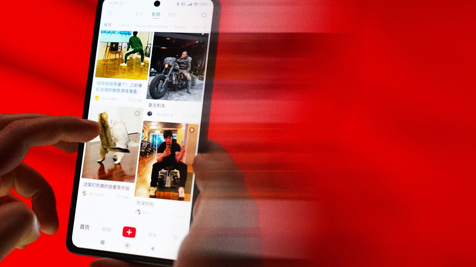 A person’s hand holds a smartphone displaying a social media feed with blurred red background.
