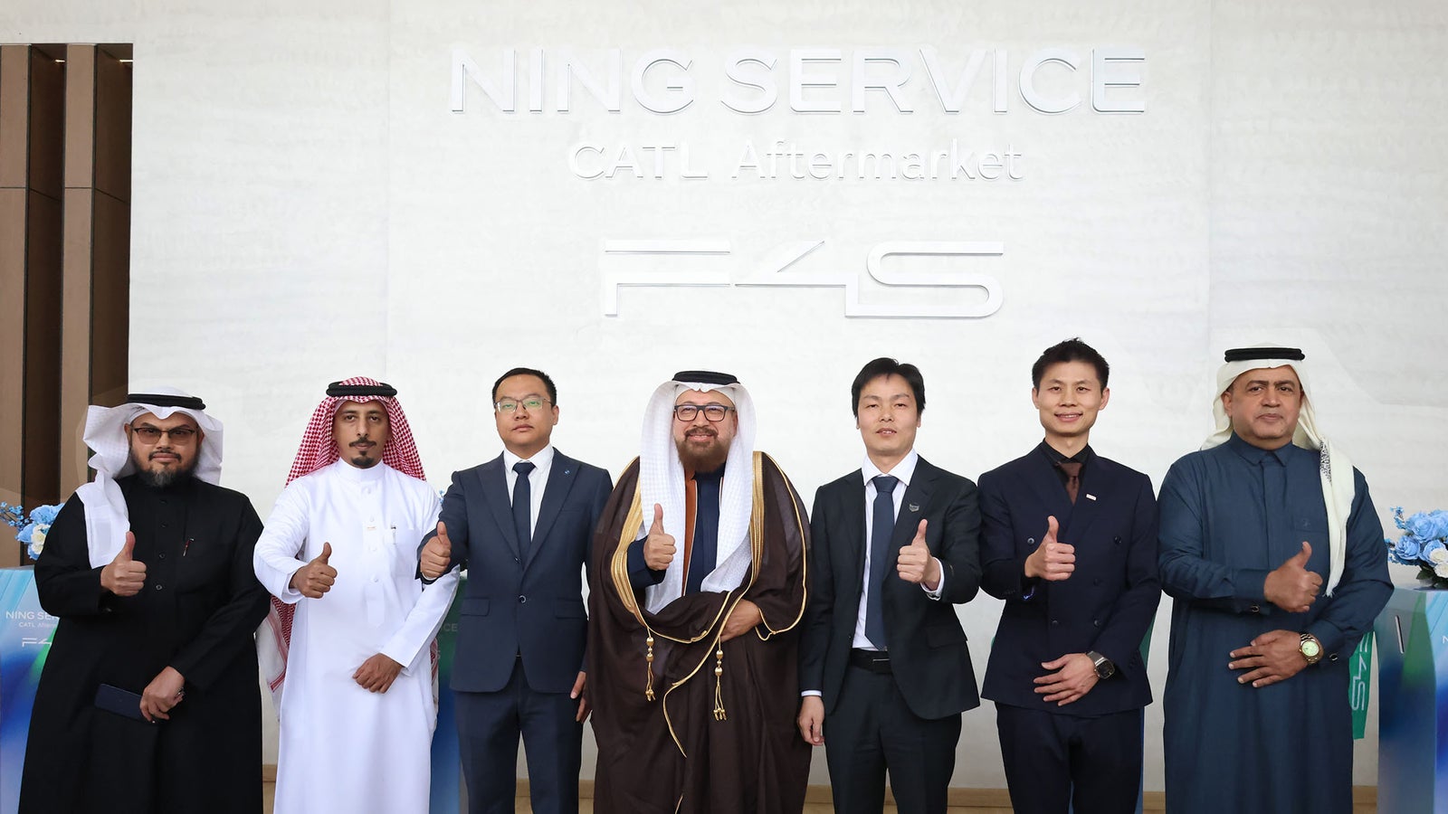 A group of six men in formal attire, posing together and giving thumbs up, with a sign reading "Ning Service CATL Aftermarket F4S" in the background.