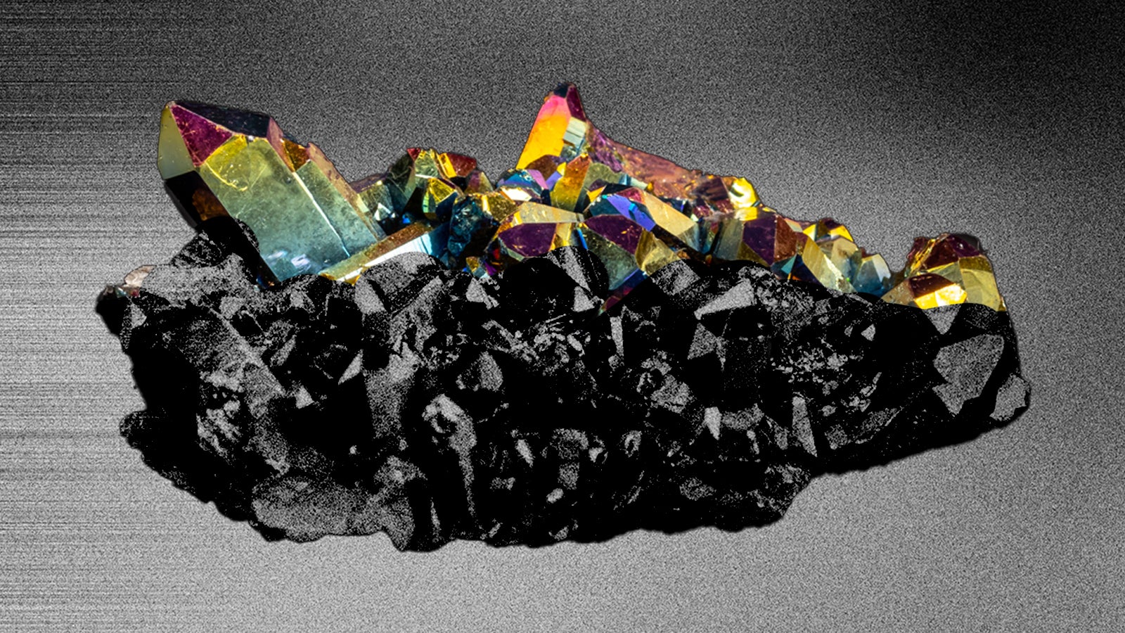 Colorful crystal cluster with sharp edges set against a dark, textured background, showcasing iridescent reflections.