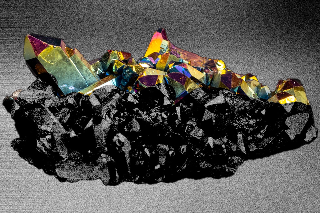 Colorful crystal cluster with sharp edges set against a dark, textured background, showcasing iridescent reflections.