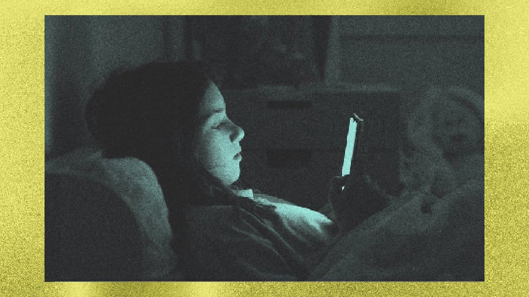 A person in bed looking intently at a phone screen, illuminated by its glow in a dimly lit room.
