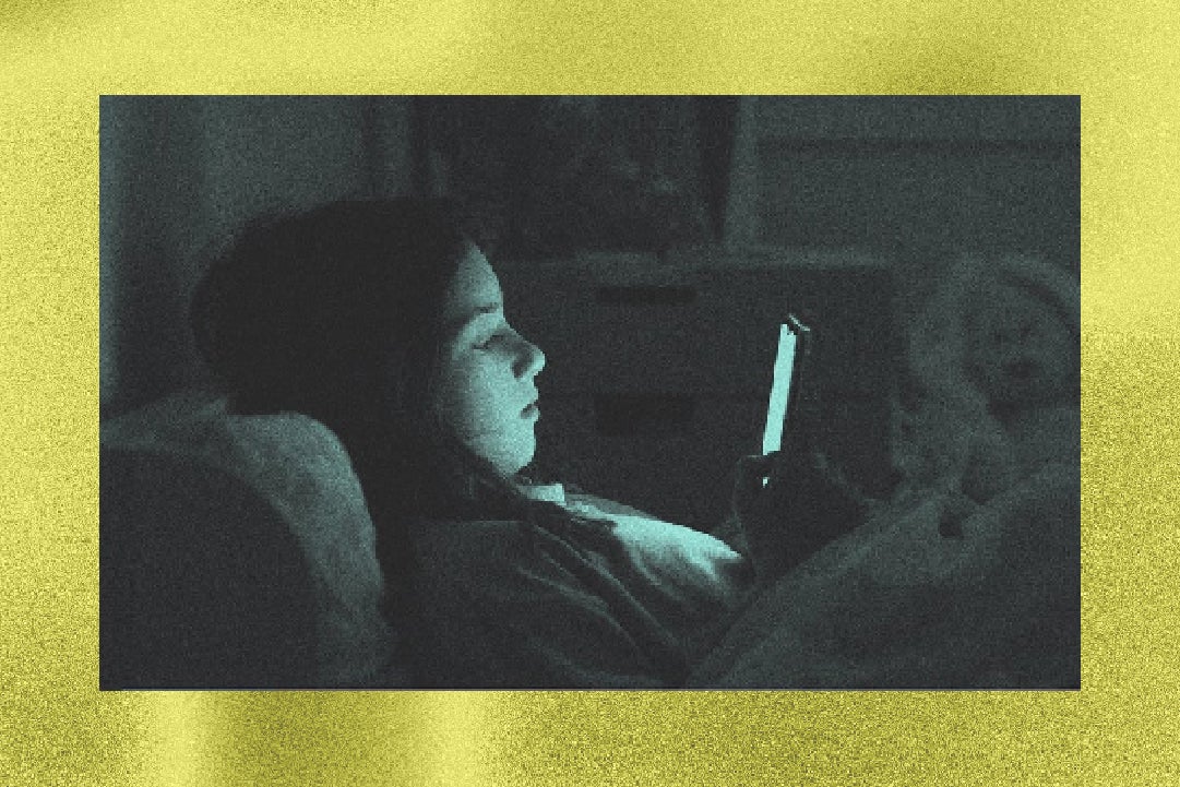 A person in bed looking intently at a phone screen, illuminated by its glow in a dimly lit room.