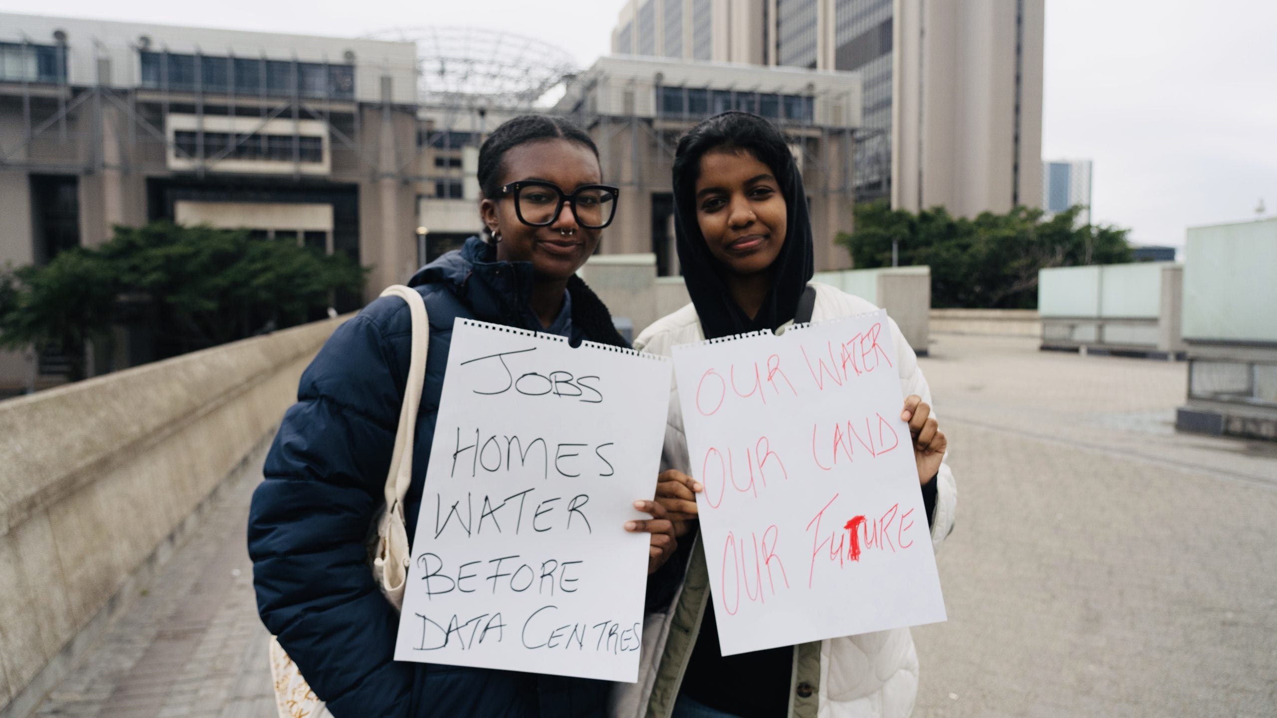 Two young women hold signs protesting for priorities such as jobs, homes, and water over data centers